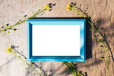 Ahşap bir yüzeyde mavi ahşap çerçeve, çerçevenin etrafında sarı çiçekler. Çerçevedeki bir yazı için boş alan