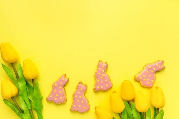 Osterflach lag es. Hausgemachte Plätzchen in Form von Hasen mit Tulpen auf gelbem Hintergrund, Ansicht von oben — Stockfoto