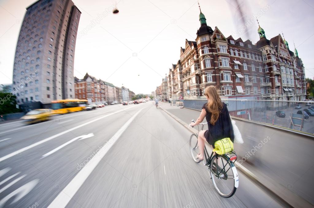 Pretty girl riding bike, old buildings around. Denmark