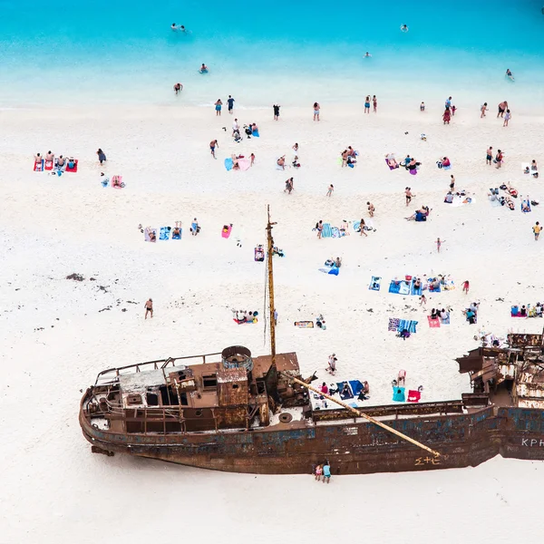 Castaways enjoying sunbathing on white sand beach near shipwreck — Stock Photo, Image