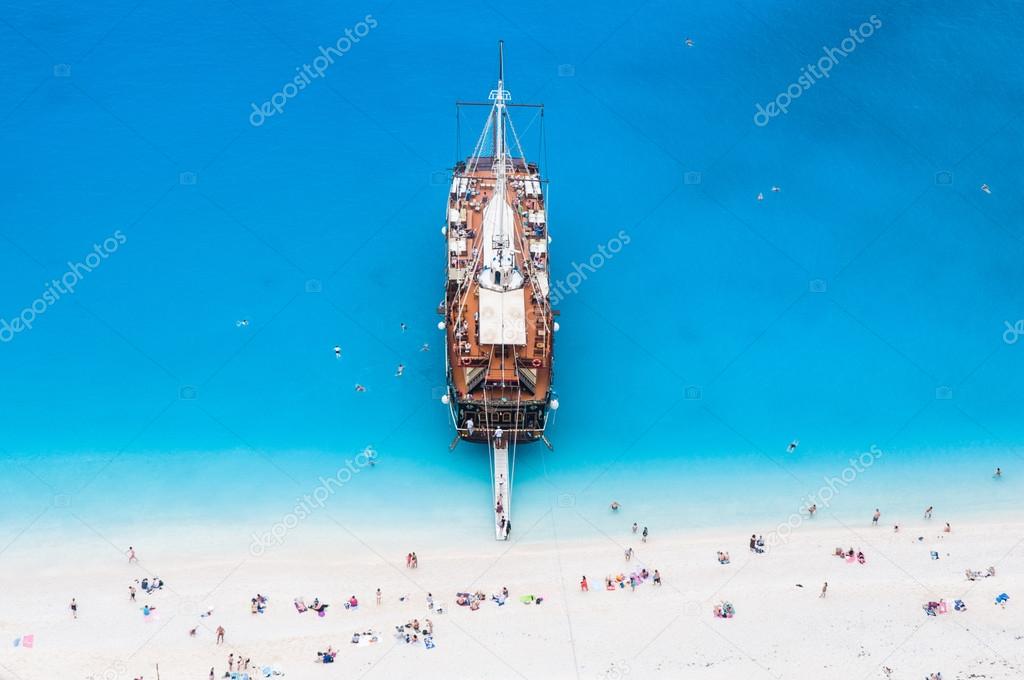 Large sail cruise ship anchored at white sand beach, seen from above