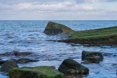 Çimento parçaları ve denizde yeşil yosunlarla kaplı büyük taşlar.