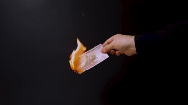 Bir adamın elinde koyu arkaplanda 100 Rus rublesinden oluşan yanan bir banknot var. 4k video