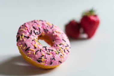Pembe kremalı bir donutun fotoğrafı, küçük bir kısmı odak noktasında ve arka planda çilekli, çok bulanık. Işık arkaplanındaki tüm nesneler