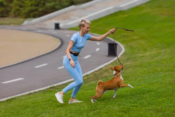 Mädchen läuft mit Hund im Park auf der Liegewiese bei Sonnenuntergang, geht mit einem Haustier in der Natur spazieren. — Stockfoto