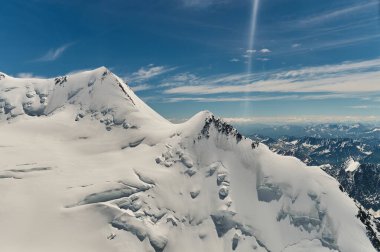 Karla kaplı dağ duvarının minimalist manzarası kalın alçak bulutların altında gün ışığında. Mavi gökyüzündeki yoğun bulutların arasında beyaz-kar zirvesi olan manzaralı parlak dağ manzarası. Karlı üstüyle harika bir manzara.