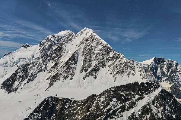 Karla kaplı dağ duvarının minimalist manzarası kalın alçak bulutların altında gün ışığında. Mavi gökyüzündeki yoğun bulutların arasında beyaz-kar zirvesi olan manzaralı parlak dağ manzarası. Karlı üstüyle harika bir manzara.