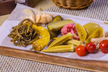 Beyaz bir tabakta farklı türde sebze turşusu. Salatalık turşusu, domates kirazı, yeşillik, mantar ve soğanlı sarımsak..