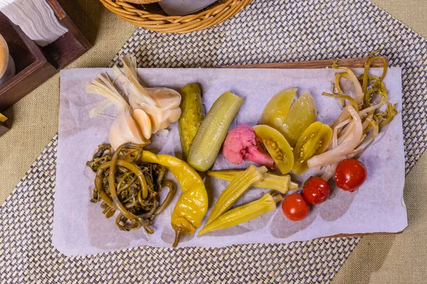 Diferentes tipos de verduras en vinagre en un plato blanco. Pepinos en escabeche, cereza de tomate, verduras, champiñones y ajo con cebolla y lechuga sobre la mesa. —  Fotos de Stock