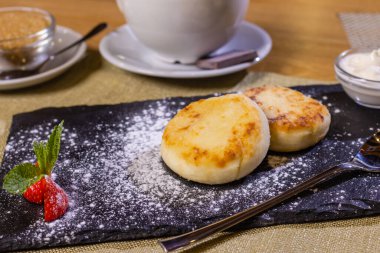 Çilekli peynirli kek. Siyah tepside iki kızarmış kaymak. Yakın plan..