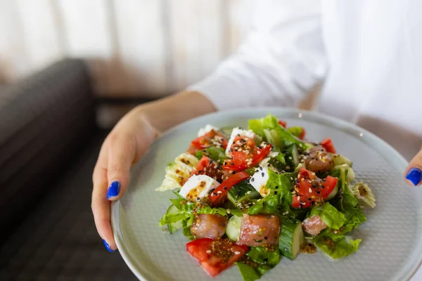 Молодая официантка держит в руках тарелку с греческим салатом. — стоковое фото