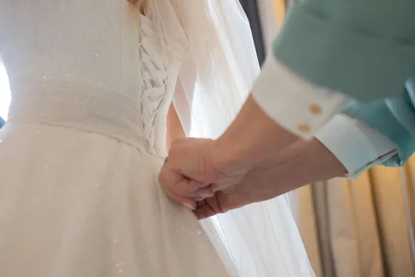 Деталь рук подружек невесты дергая ленту невесты корсет свадебного платья во время одевания. — стоковое фото
