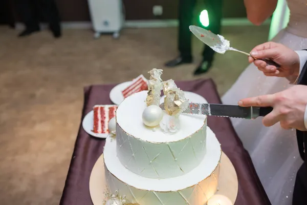 Mains de mariée et marié coupé d'une tranche d'un gâteau de mariage. — Photo