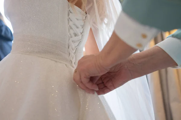 Detalhe de damas de honra mãos puxando fita de saturação de noivas vestido de noiva espartilho durante o curativo. — Fotografia de Stock