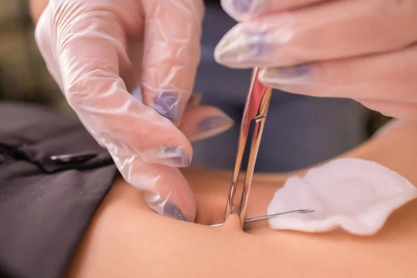 De eerste piercing. Omhoog het kleden van haar nieuwe oorbellen op de navel. Vrouwelijke piercing. — Stockfoto