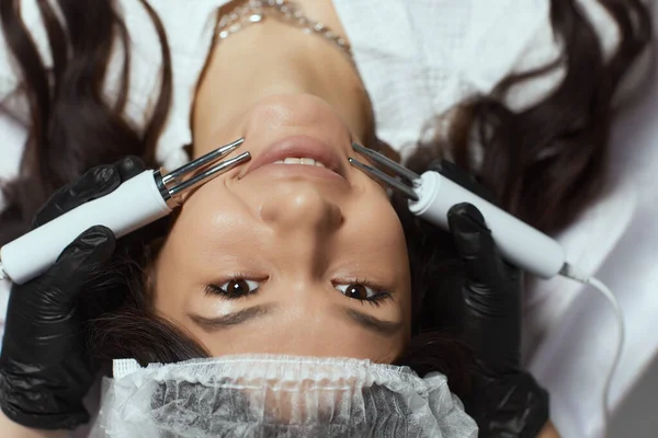 Cosmetologia. Mulher bonita na clínica do spa que recebe estimulando o tratamento facial elétrico do terapeuta . — Fotografia de Stock