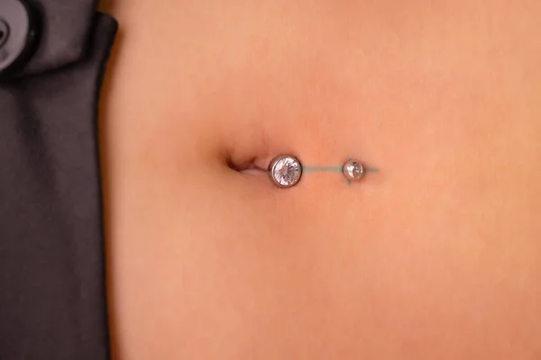 O primeiro piercing. A vestir os brincos no umbigo. Piercing feminino . — Fotografia de Stock