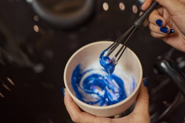 Ellerinde fırça tutan ve saç boyasını yakından karıştıran beyaz lastik eldivenli bir kız..