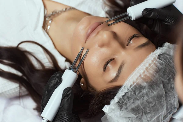Kosmetika. Krásná žena na lázeňské klinice dostávají stimulující elektrické ošetření obličeje od terapeuta. — Stock fotografie