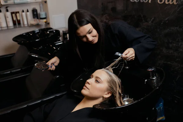 Hairdresser in beauty salon washes his client hair, before procedure of applying natural restoring ingredients and vitamins to hair and haircut. — Stockfoto