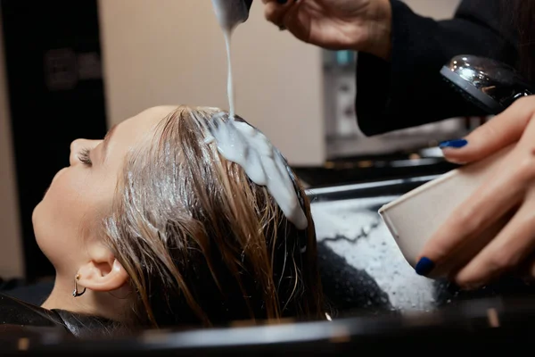 Kapster in schoonheidssalon wast zijn klant haar, voor de procedure van het aanbrengen van natuurlijke restauratie ingrediënten en vitaminen op haar en kapsel. — Stockfoto