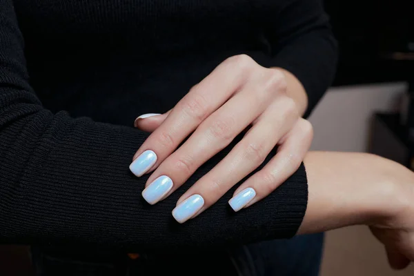 Vacker manikyr. Nagellack som appliceras på hand, lack är en blå färg. Blå bakgrund närbild. — Stockfoto