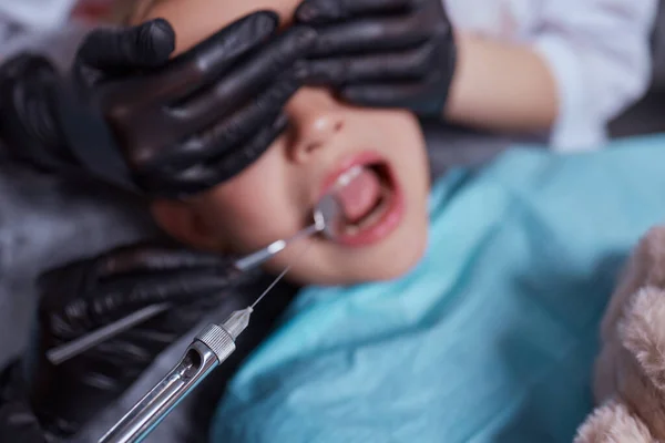 Caucasian young child girl sitting in medical chair while dentist fixing teeth at dental clinic using dental tools instruments, close-up photo of face. professional medical specialist. — Foto Stock