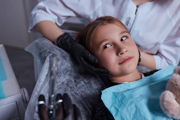 Caucasian young child girl sitting in medical chair while dentist fixing teeth at dental clinic using dental tools instruments, close-up photo of face. professional medical specialist. — Foto Stock