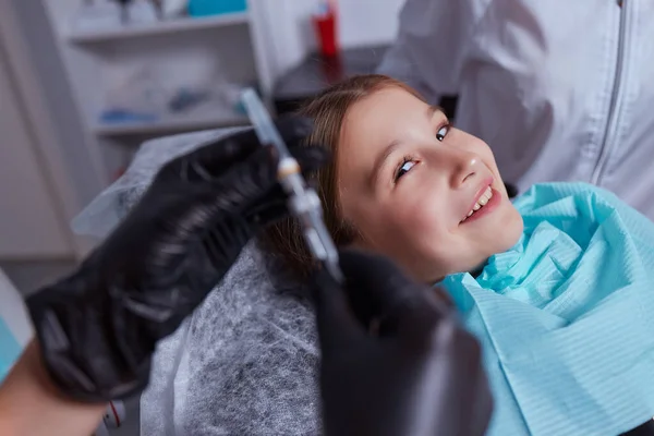 Una ragazzina dallo studio dentistico, che fa l'iniezione di anestesia locale nelle gengive. Vista ritagliata del dentista gengive intorpidite per il lavoro dentale. Concetto di cura dentale pediatrica. — Foto Stock