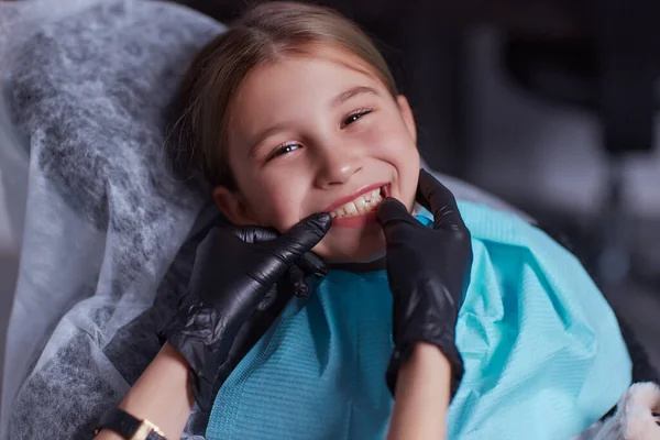 Caucasian young child girl sitting in medical chair while dentist fixing teeth at dental clinic using dental tools instruments, close-up photo of face. professional medical specialist. — Foto Stock