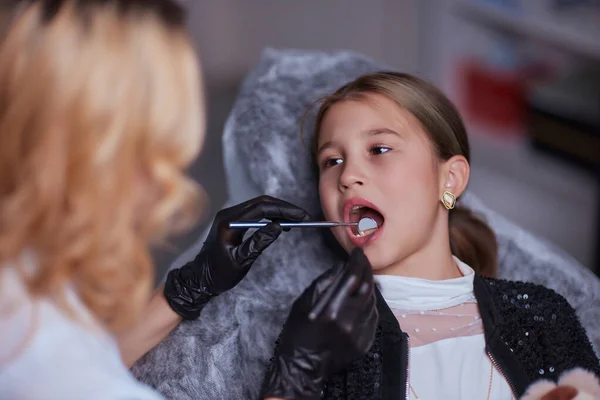 Caucasian young child girl sitting in medical chair while dentist fixing teeth at dental clinic using dental tools instruments, close-up photo of face. professional medical specialist. — Foto Stock