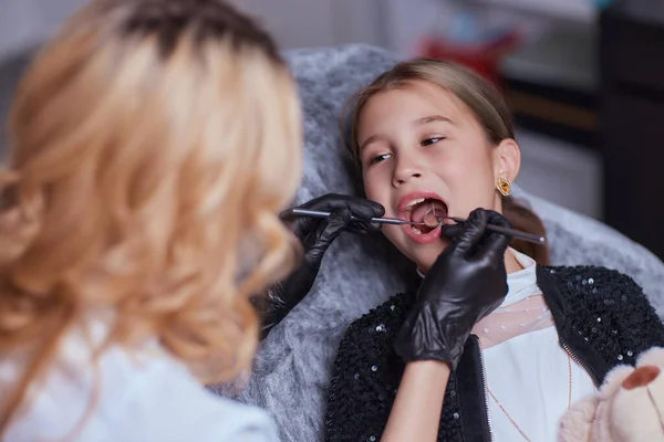 Kaukasisches kleines Mädchen, das im Behandlungsstuhl sitzt, während der Zahnarzt die Zähne in der Zahnklinik mit zahnärztlichen Instrumenten repariert, Nahaufnahme des Gesichts. Facharzt für Allgemeinmedizin. — Stockfoto