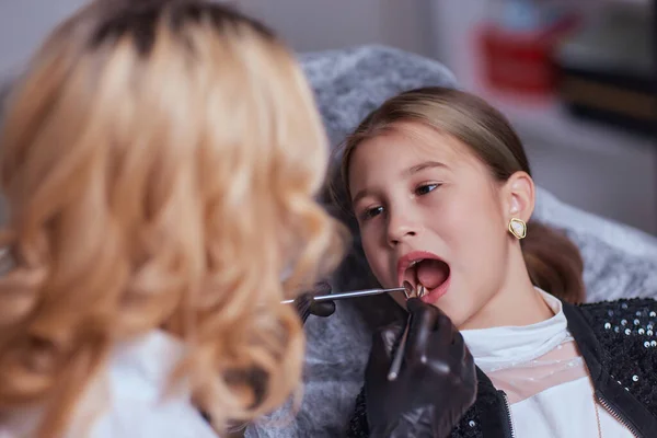 Kaukasisches kleines Mädchen, das im Behandlungsstuhl sitzt, während der Zahnarzt die Zähne in der Zahnklinik mit zahnärztlichen Instrumenten repariert, Nahaufnahme des Gesichts. Facharzt für Allgemeinmedizin. — Stockfoto
