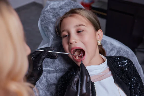 카프카스 출신의 어린 소녀가 의료용 의자에 앉아 치과에서 치과용 도구를 사용 해 치아를 치료하고 있습니다. 얼굴을 확대 한 사진이죠. 전문 의료 전문가. — 스톡 사진