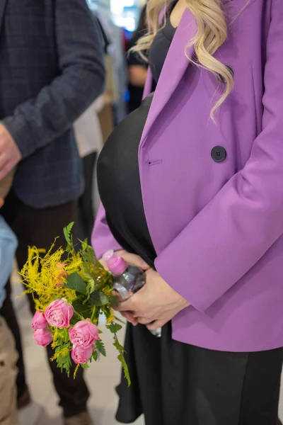 Zbliżenie piękne kobiety w ciąży s brzuch, trzymając kwiaty w rękach. — Zdjęcie stockowe