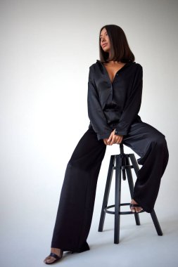 Young slim woman model in sunglasses, black military uniform stands with her legs wide apart and arms crossed at chest.