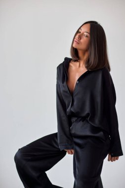 Young slim woman model in sunglasses, black military uniform stands with her legs wide apart and arms crossed at chest.