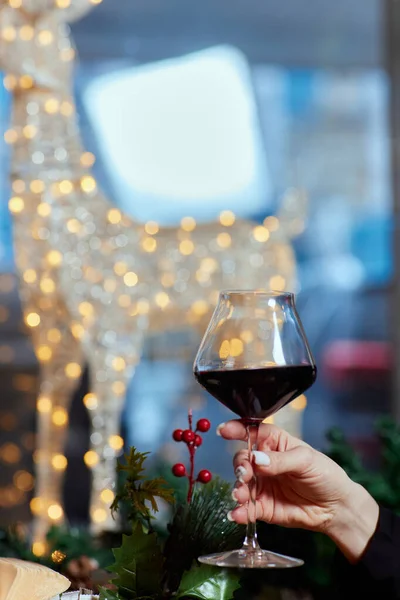 クリスマスツリーを背景にシャンパンのグラスを持つ女性の手、クリスマスだけのコンセプト、クローズアップを祝う. — ストック写真