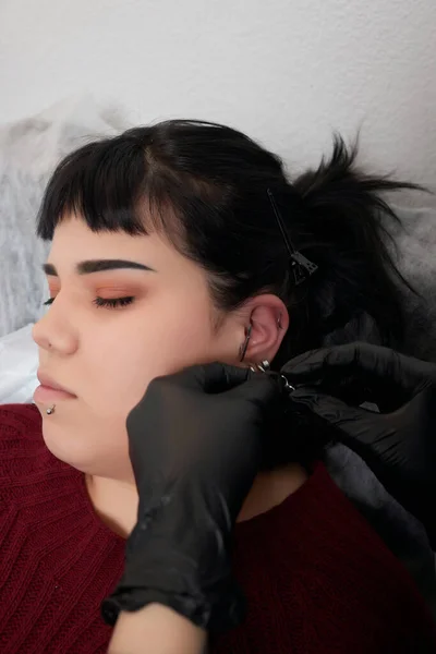 Professionale tenendo il gioiello del piercing giorno poco prima di avvitare la palla. Tipo tragus. — Foto Stock