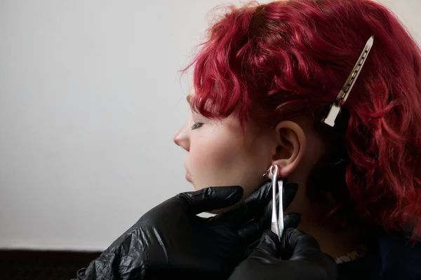 Um esteticista faz uma punção do lóbulo da orelha com um dispositivo descartável em um salão de beleza. Orelha lóbulo perfurante. — Fotografia de Stock