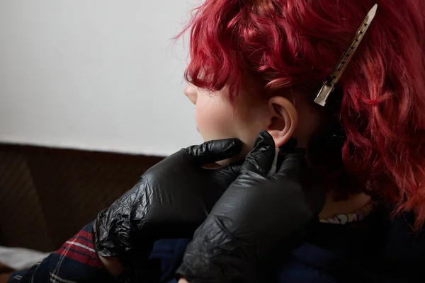 En kosmetolog gör en punktering av örsnibben med en engångsenhet i en skönhetssalong. Öron piercing lob. — Stockfoto