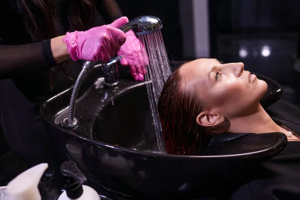 Peluquería en el salón de belleza lava el cabello de su cliente, antes del procedimiento de aplicación de ingredientes naturales de restauración y vitaminas para el cabello y corte de pelo. — Foto de Stock