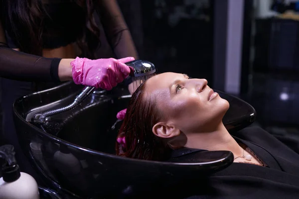 Парикмахер в салоне красоты моет волосы своему клиенту, перед процедурой нанесения натуральных восстанавливающих ингредиентов и витаминов на волосы и стрижку. — стоковое фото
