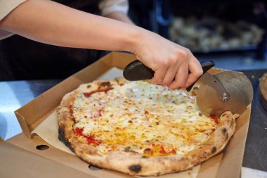 Mutfakta pizza kesen beyaz üniformalı aşçının yakın çekimi..
