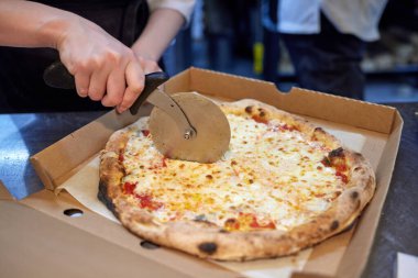 Mutfakta pizza kesen beyaz üniformalı aşçının yakın çekimi..