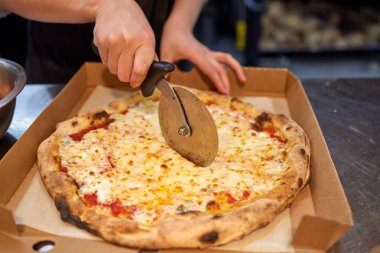 Mutfakta pizza kesen beyaz üniformalı aşçının yakın çekimi..