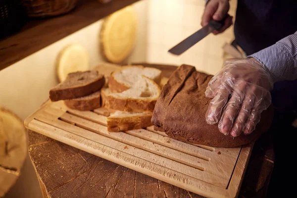 Αρσενικό χέρια κοπής σταρένιο ψωμί στο ξύλινο ταμπλό, επιλεκτική εστίαση. — Φωτογραφία Αρχείου