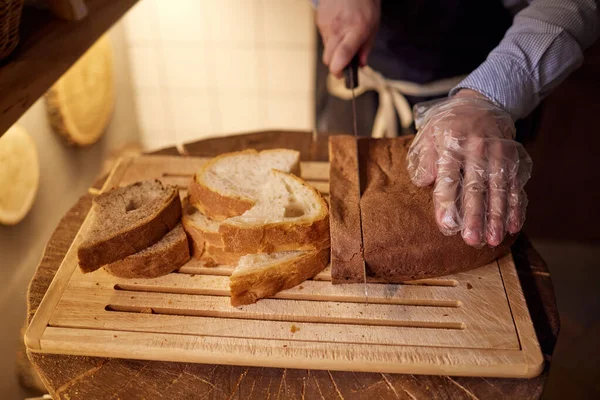 Αρσενικό χέρια κοπής σταρένιο ψωμί στο ξύλινο ταμπλό, επιλεκτική εστίαση. — Φωτογραφία Αρχείου