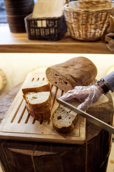 Manos masculinas cortando pan de trigo en el tablero de madera, enfoque selectivo . — Foto de Stock