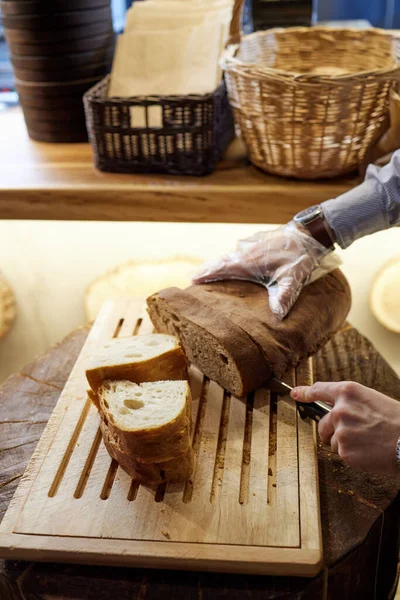 Manos masculinas cortando pan de trigo en el tablero de madera, enfoque selectivo . — Foto de Stock